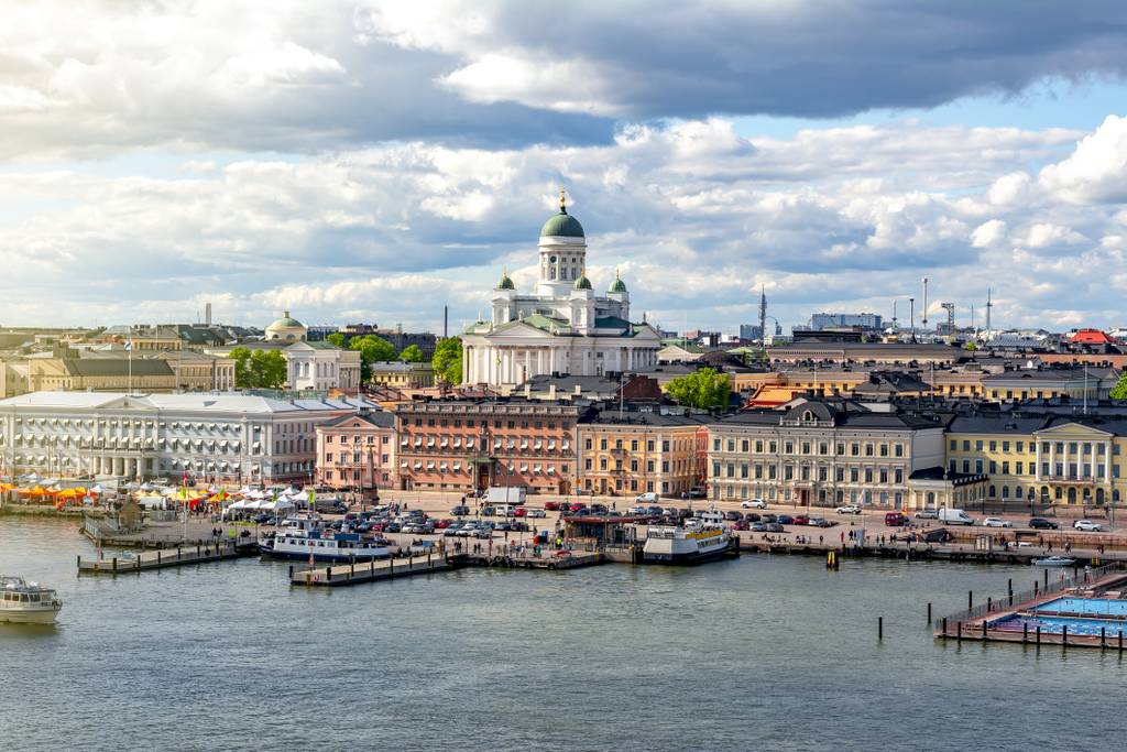 A coastal cityscape with vibrant buildings, a prominent cathedral, and bustling harbor under a partly cloudy sky.
