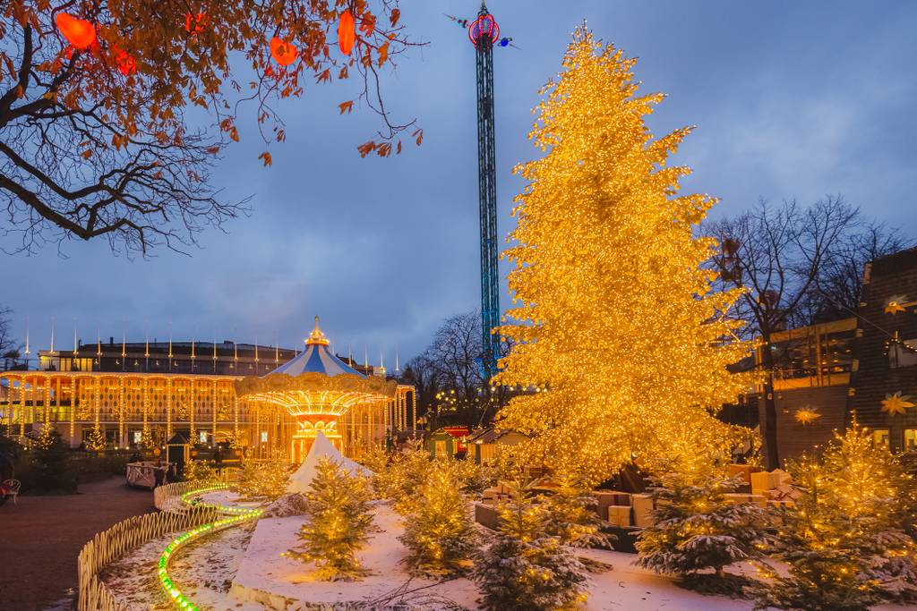 Beleuchteter Vergnügungspark mit einem großen, leuchtenden Weihnachtsbaum, einem Karussell und festlicher Dekoration unter einem dämmrigen Abendhimmel.