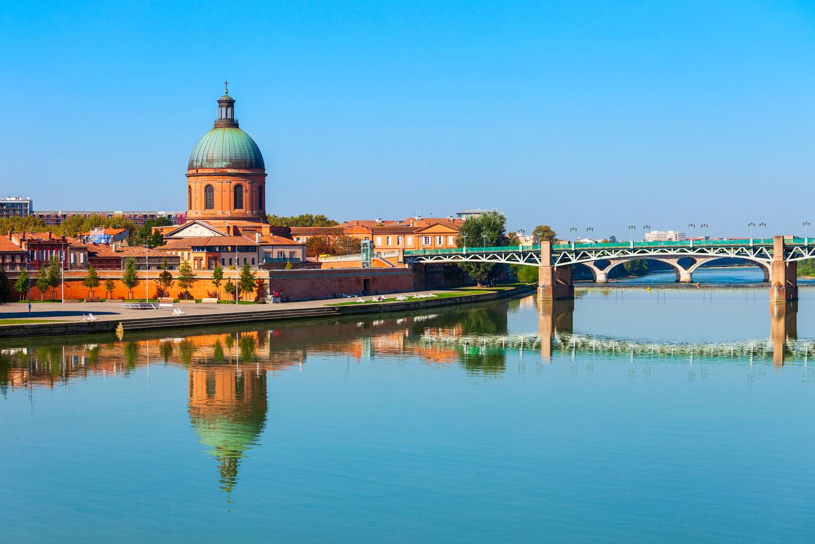 Dome of La Grave hospital and Pont Saint-Pierre bridge reflected in the Garonne River under a clear blue sky in Toulouse, France.