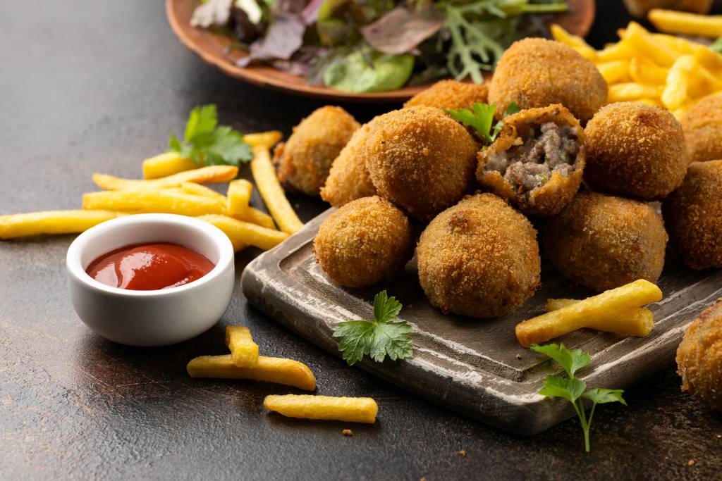 Polpette impanate su un vassoio con patatine fritte, ketchup e un piatto di insalata mista sullo sfondo.