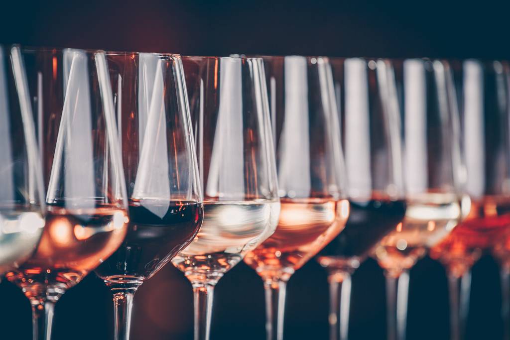 Eine Reihe von Weingläsern mit verschiedenen Rot-, Rosé- und Weißweinen, dicht nebeneinander vor dunklem Hintergrund angeordnet