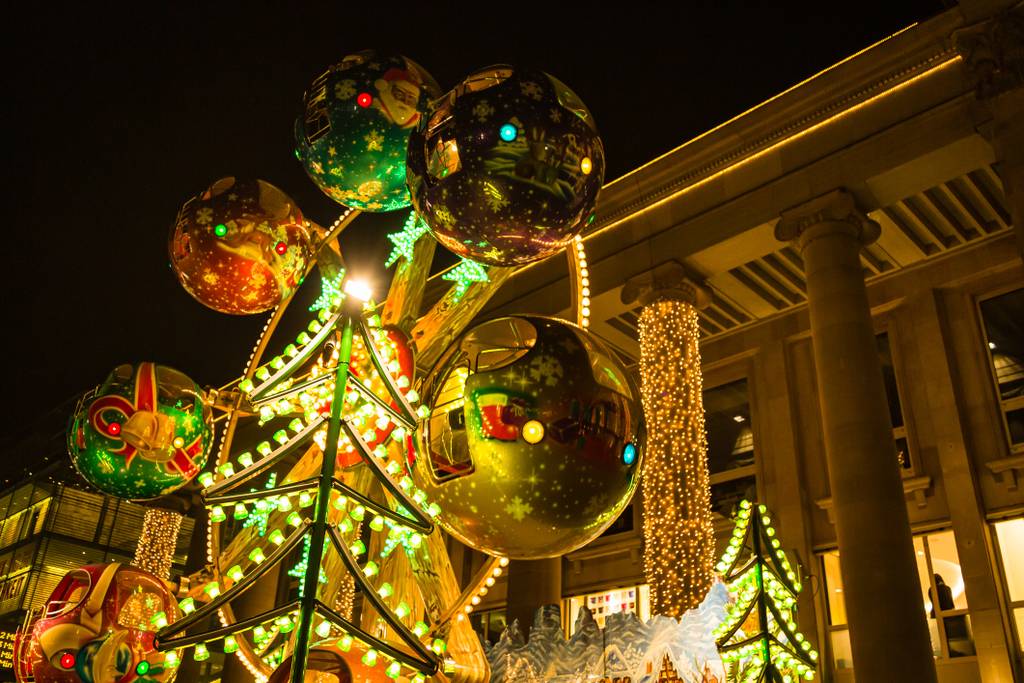 Festliche Weihnachtsdekoration mit großen, beleuchteten Ornamenten und Lichtern vor einem Gebäude mit Säulen und funkelnder Beleuchtung.