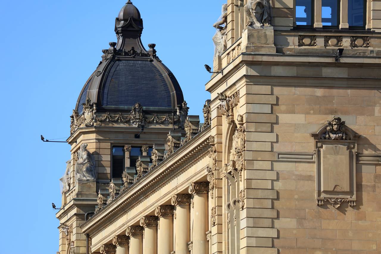 Prächtige Steinfassade mit Säulen und detaillierten Skulpturen, gekrönt von einer Kuppel vor klarem blauen Himmel.