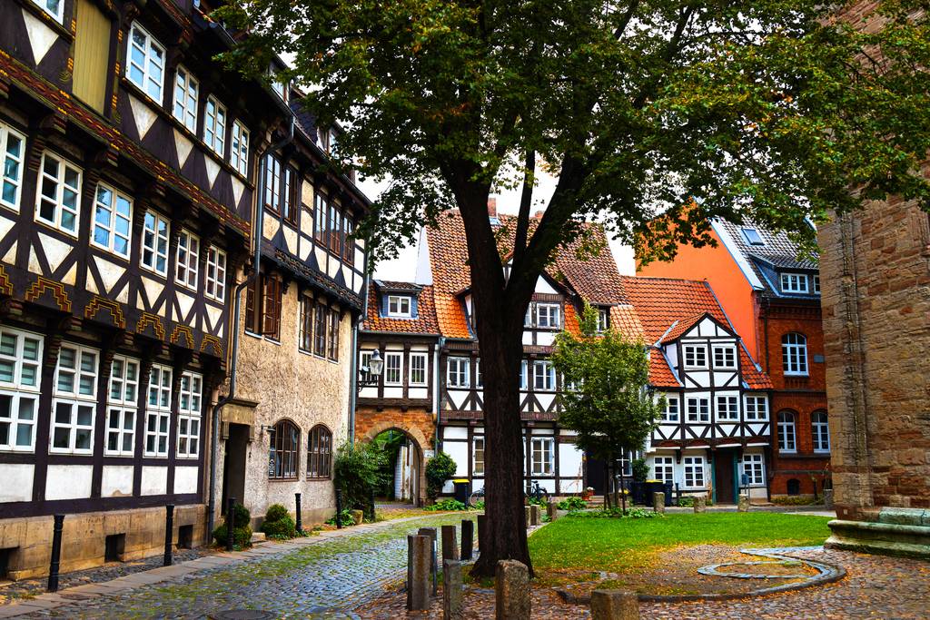 Historischer deutscher Innenhof mit Fachwerkhäusern, Kopfsteinpflasterweg und einem großen Baum in der Mitte.