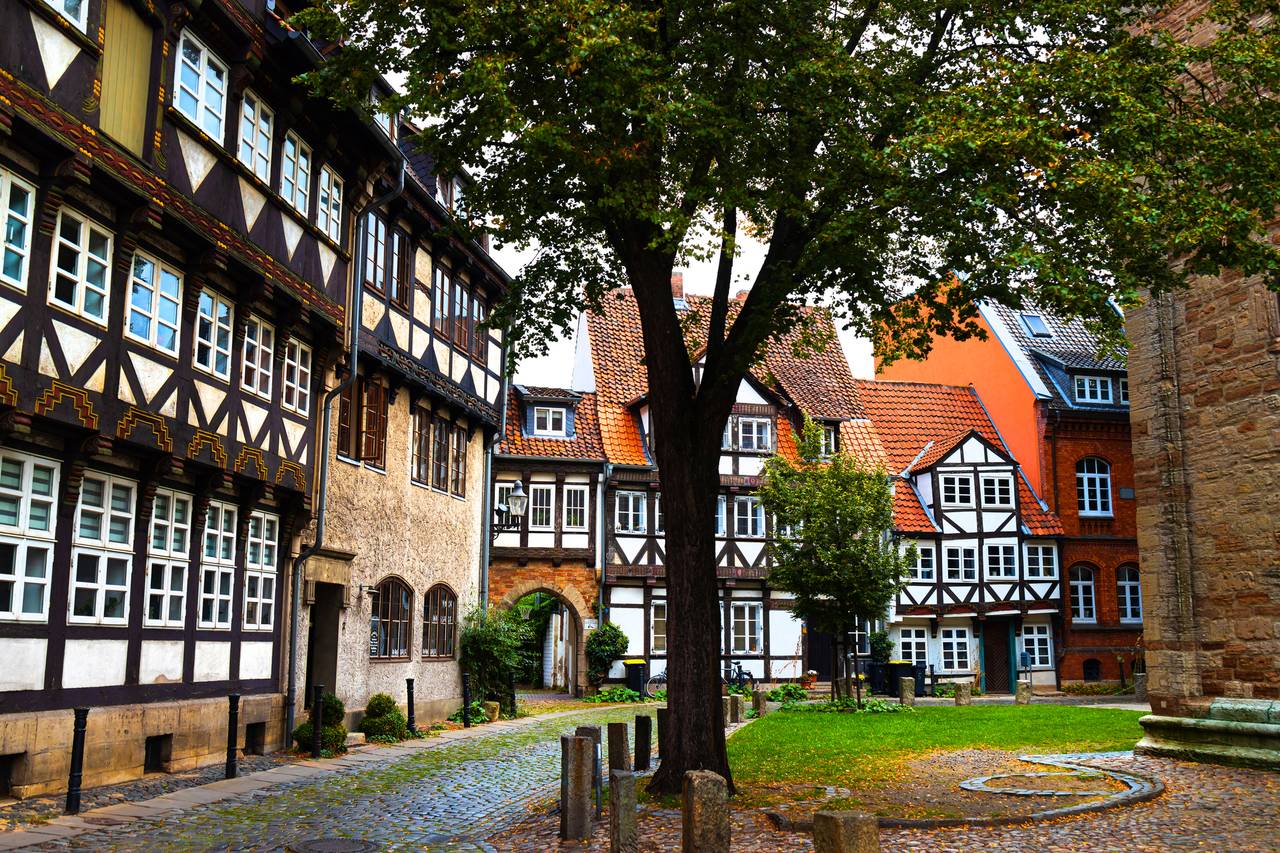 Historischer deutscher Innenhof mit Fachwerkhäusern, Kopfsteinpflasterweg und einem großen Baum in der Mitte.