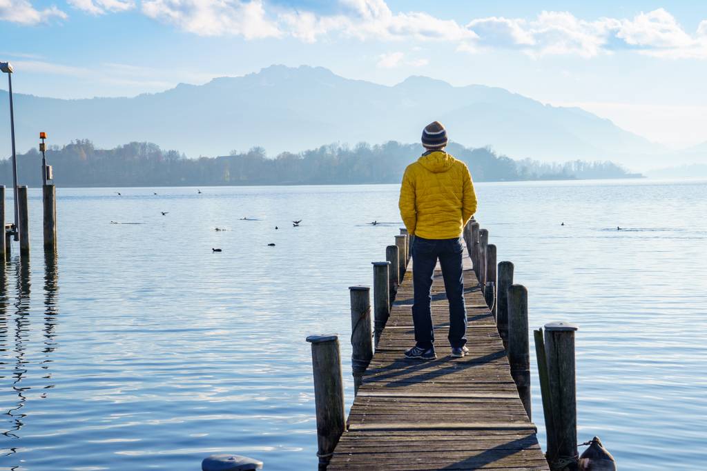 Mann mit gelber Jacke auf Bootssteeg blickt auf die Bergwelt rund um den Chiemsee