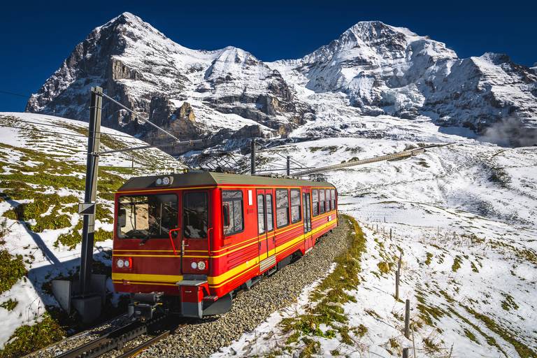 Roter Zahnradbahn-Zug fährt auf Schienen durch verschneite Alpengleise, im Hintergrund ragen imposante, schneebedeckte Gipfel empor.