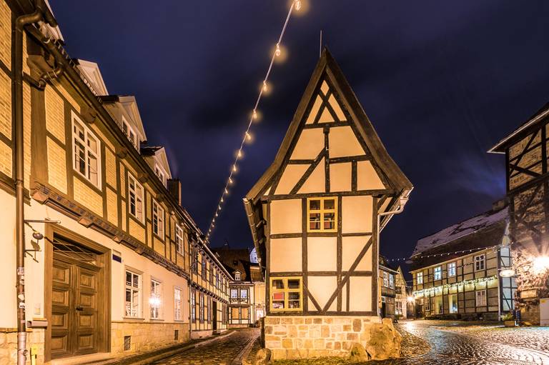 Fachwerkhäuser an einer Kopfsteinpflasterstraße bei Nacht, beleuchtet von Lichterketten, in einer malerischen europäischen Kleinstadt.