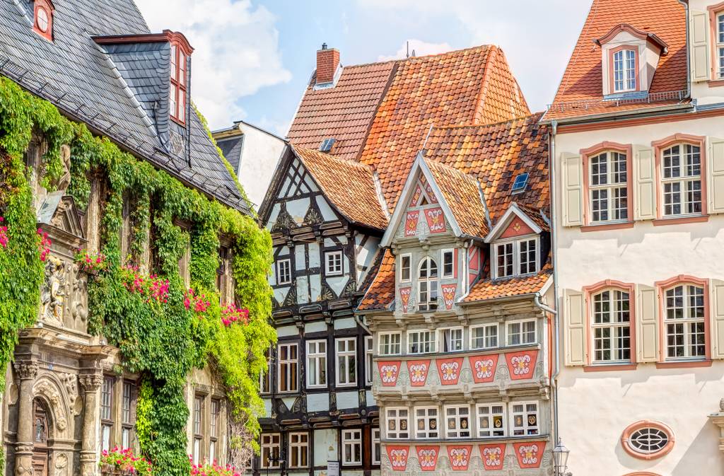Bunte, historische europäische Gebäude mit kunstvoll verzierten Fassaden und roten Ziegeldächern, geschmückt mit Grünpflanzen und Blumen, unter einem teilweise bewölkten Himmel
