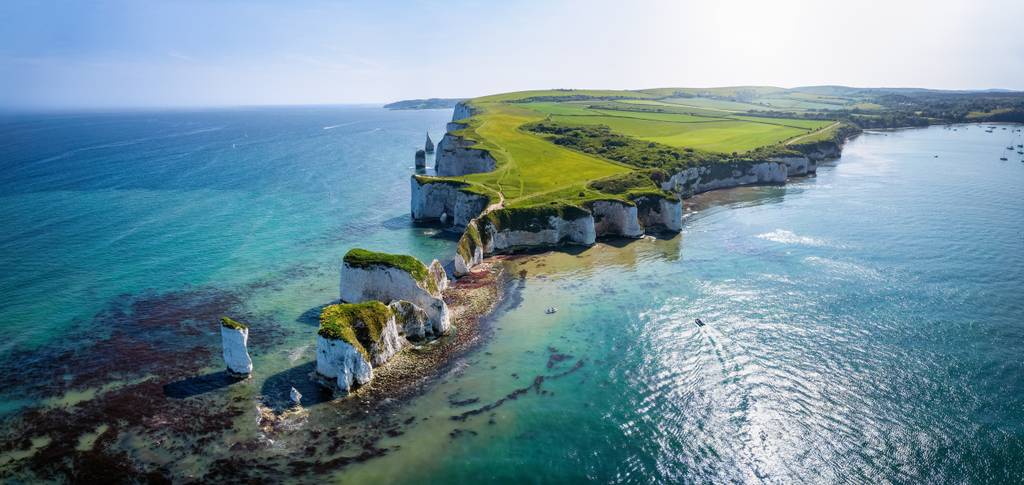 Aerial view of a coastal landscape with white chalk cliffs, green fields, and blue sea under a clear sky.