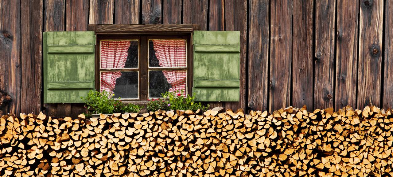 Blick auf ein Fenster und Brennholz vor einer Almhütte gelagert