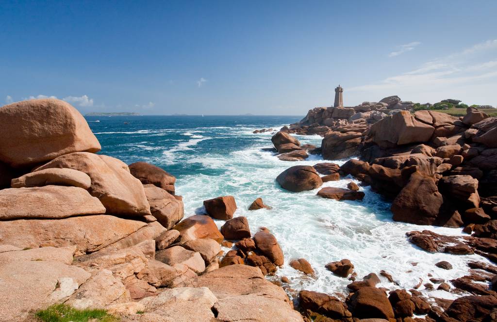 Littoral rocheux aux imposants blocs de granit rose et phare surplombant l'océan