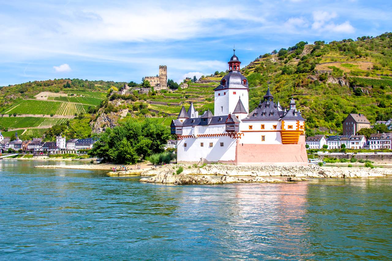 Blick auf die Burg Pfalzgrafenstein am Rhein, umgeben von Hügeln und Weinbergen unter einem leicht bewölkten Himmel