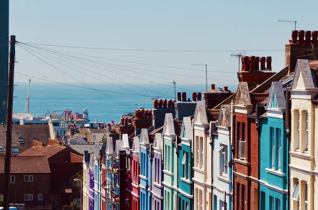 Colorful row houses on a hill of Brighton with a view of the sea in the background under a clear blue sky.