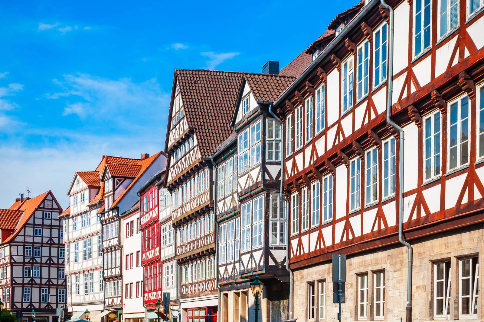 Bunte Fachwerkhäuser in einer Reihe unter blauem Himmel, mit detailreicher Holzkonstruktion und großen Fenstern