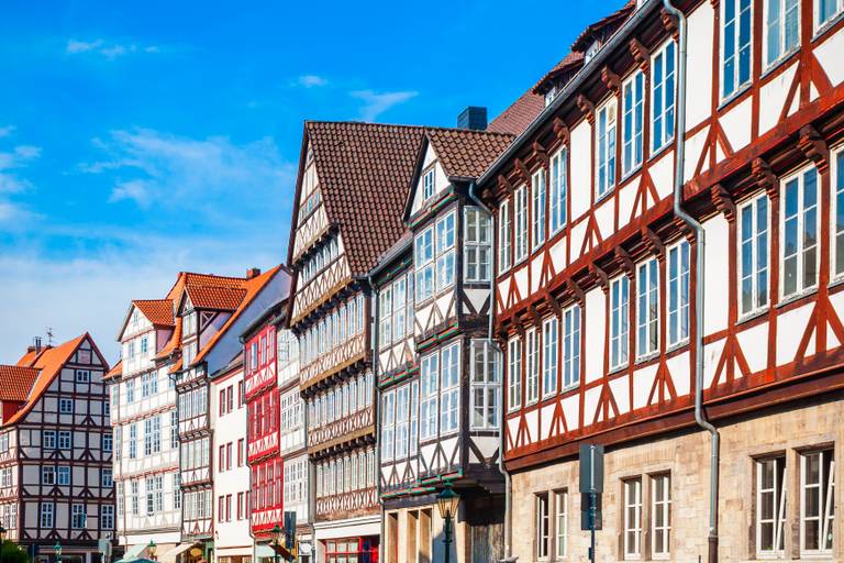 Bunte Fachwerkhäuser in einer Reihe unter blauem Himmel, mit detailreicher Holzkonstruktion und großen Fenstern