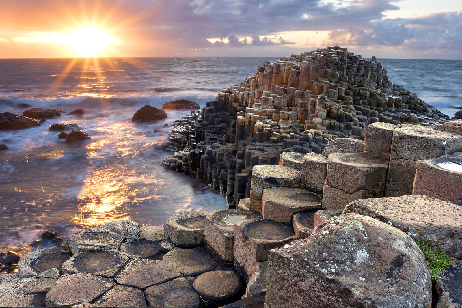 Sunset over Giant's Causeway, showcasing interlocking basalt columns by the sea, with waves gently crashing against the rocks.