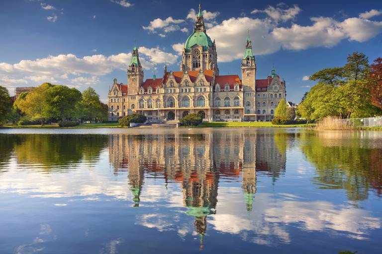 Majestätisches Gebäude mit grüner Kuppel und Türmen, spiegelt sich in einem stillen See unter einem teils bewölkten blauen Himmel