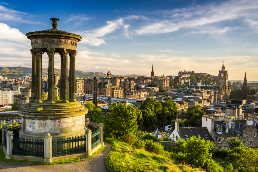 View of Edinburgh from Calton Hill, featuring the Dugald Stewart Monument in the foreground and historic city buildings under a blue sky.