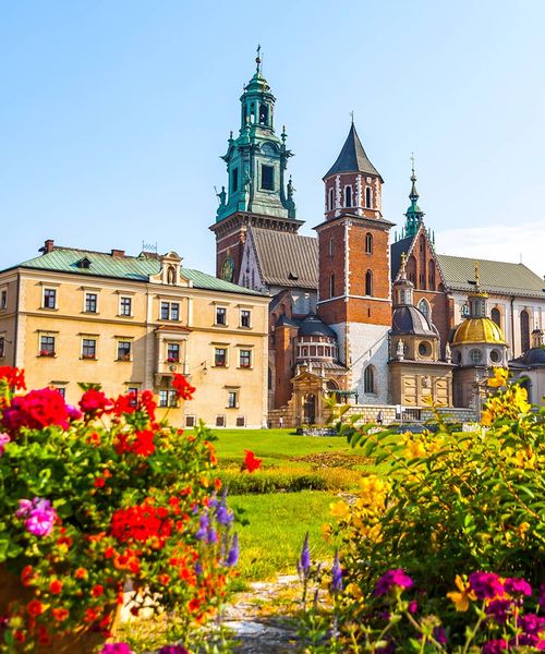 A large cathedral next to a lawn with many vibrantly colored flowers under a clear blue sky