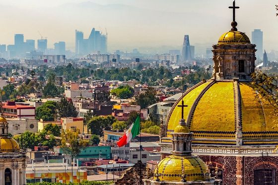 Aerial view of an ornate stone building topped with gold domes and crosses with a cityscapes in the background