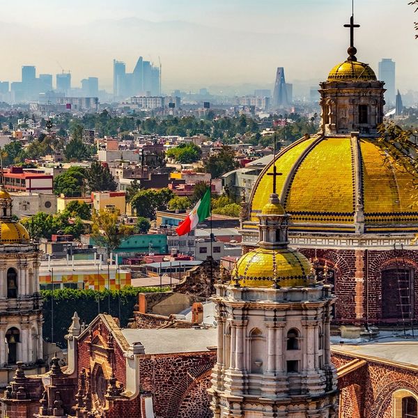 Aerial view of an ornate stone building topped with gold domes and crosses with a cityscapes in the background