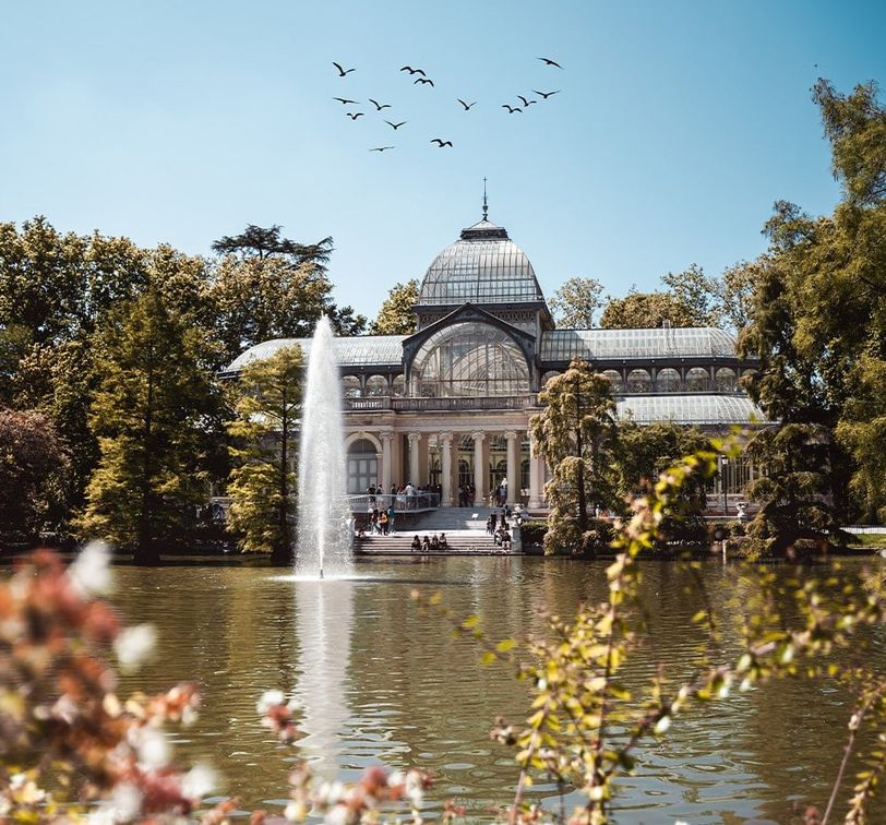 A building with many glass details situated next to the water with a fountain in front of the building