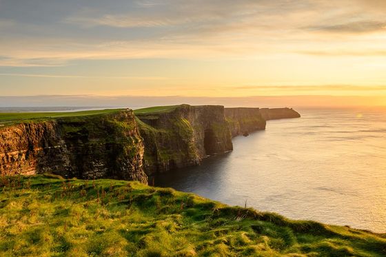 A grassy cliffside situated next to a large calm body of water during sunset