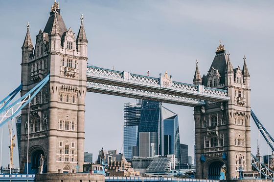 A view of the ornately detailed Tower Bridge in London over water with tall skyscrapers in the background