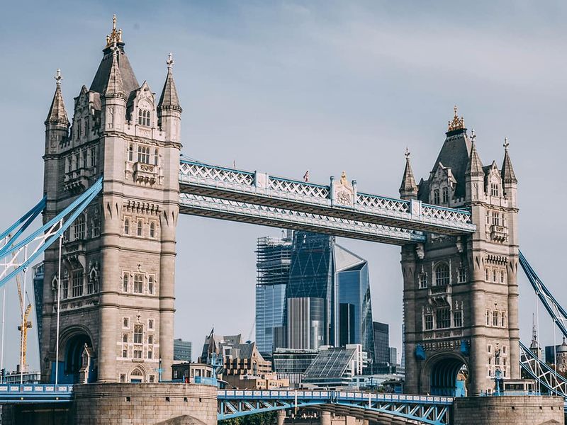 A view of the ornately detailed Tower Bridge in London over water with tall skyscrapers in the background