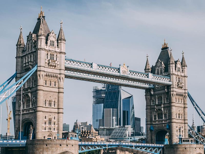 A view of the ornately detailed Tower Bridge in London over water with tall skyscrapers in the background