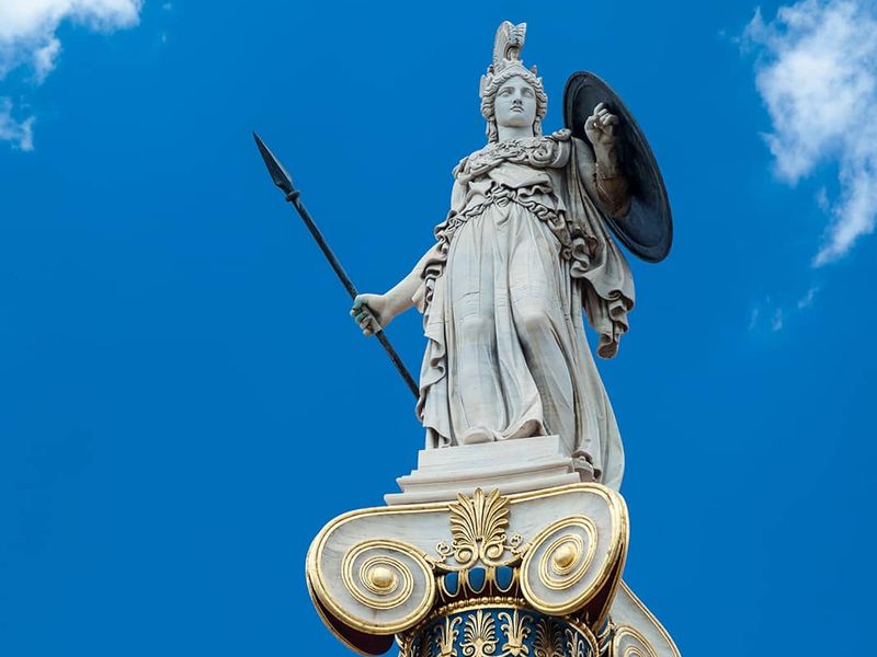 Statue of a woman wearing a helmet and holding a spear and shield atop a stone column