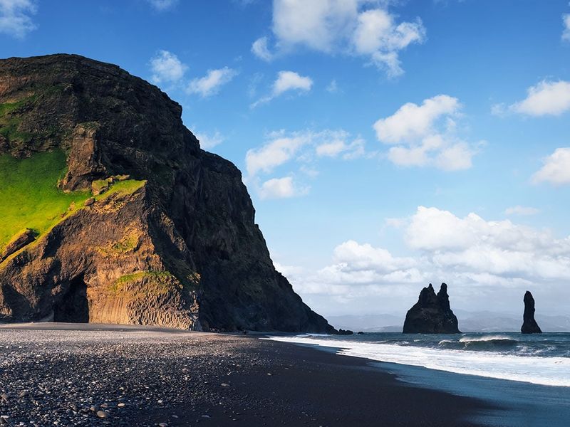 A black sand beach with dark rock formations in the water