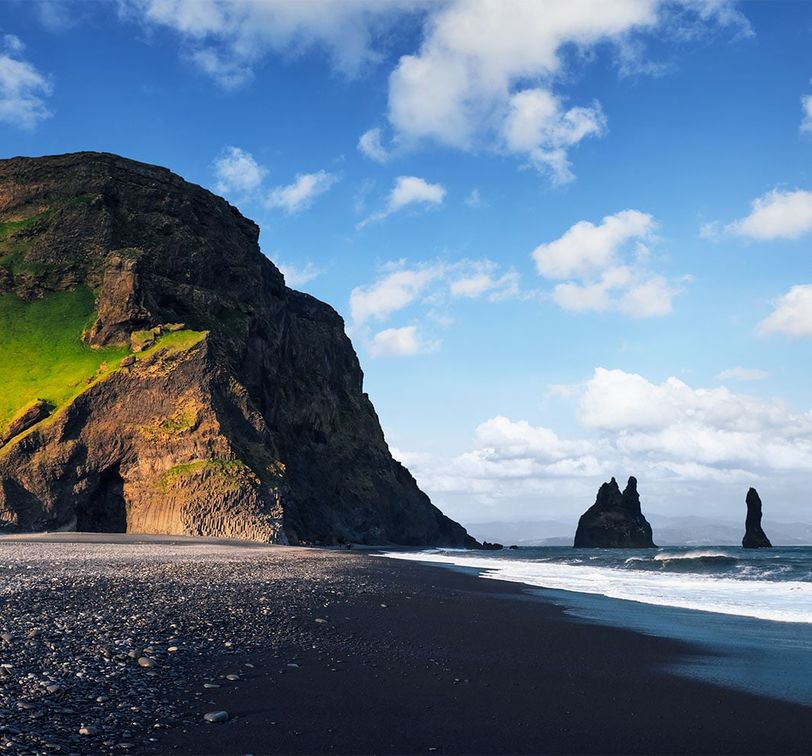 A black sand beach with dark rock formations in the water