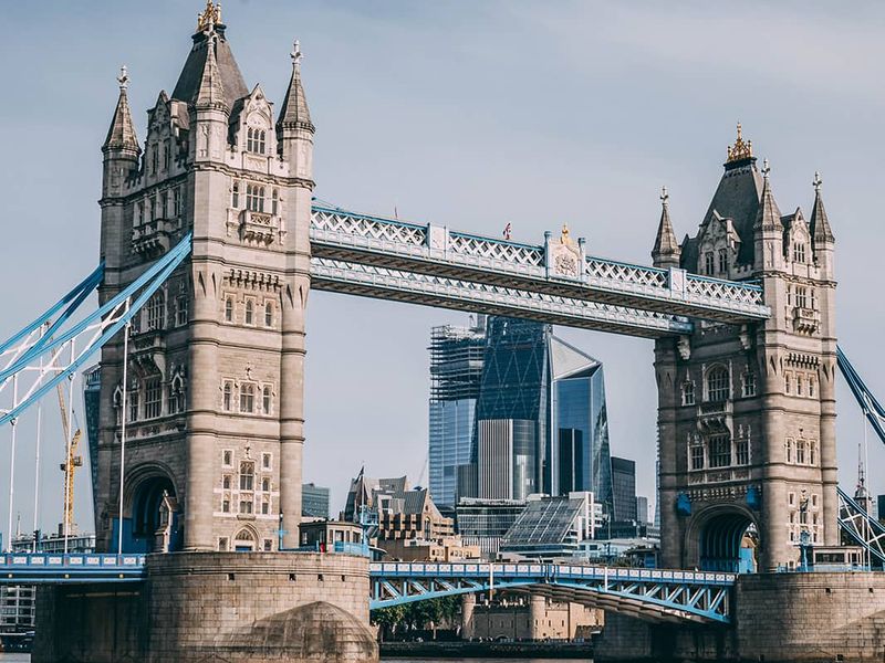 A view of the ornately detailed Tower Bridge in London over water with tall skyscrapers in the background