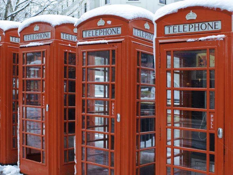 A row of red telephone booths topped with snow
