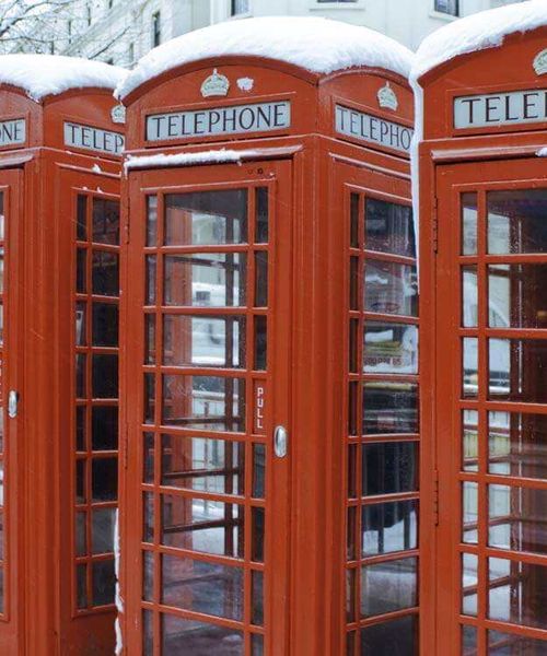 A row of red telephone booths topped with snow