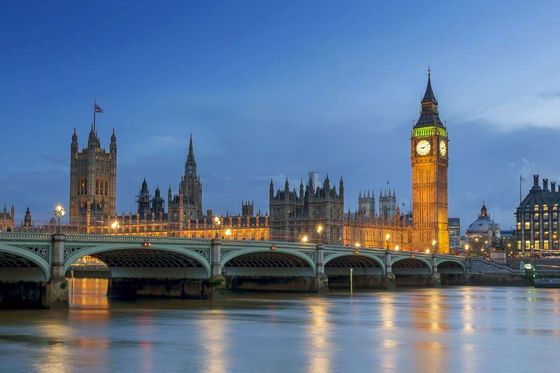 A bridge spanning a river and a large, ornate building with a clock tower behind it at dusk