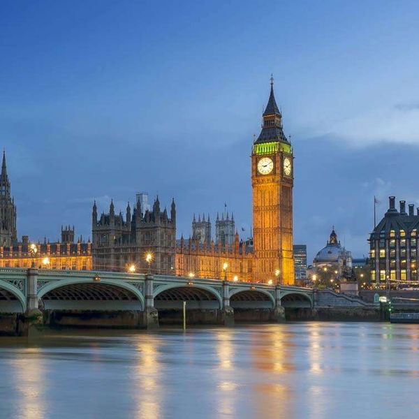 A bridge spanning a river and a large, ornate building with a clock tower behind it at dusk
