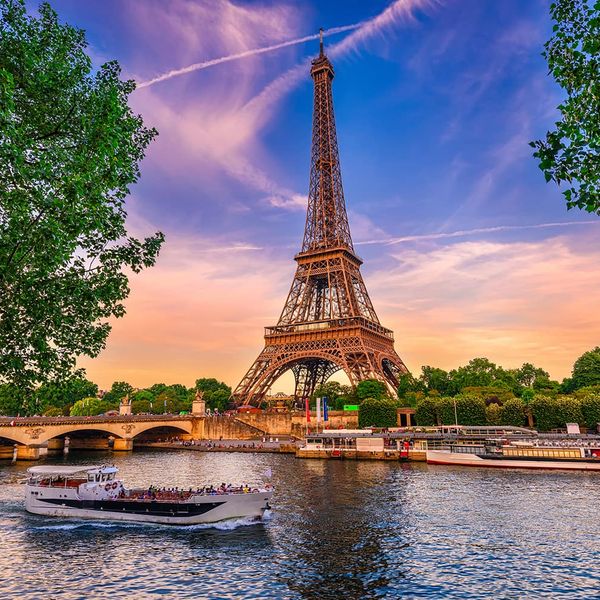 The Eiffel Tower with a vibrant sunset in the background and a body of water in the foreground with a boat passing in front