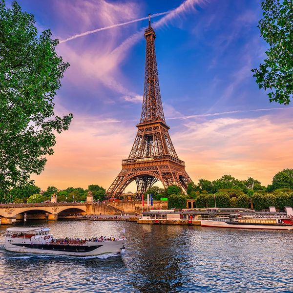 The Eiffel Tower with a vibrant sunset in the background and a body of water in the foreground with a boat passing in front