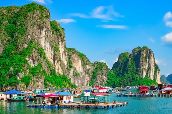 Many floating homes situated next to each other in calm waters surrounded by tall rocky islands