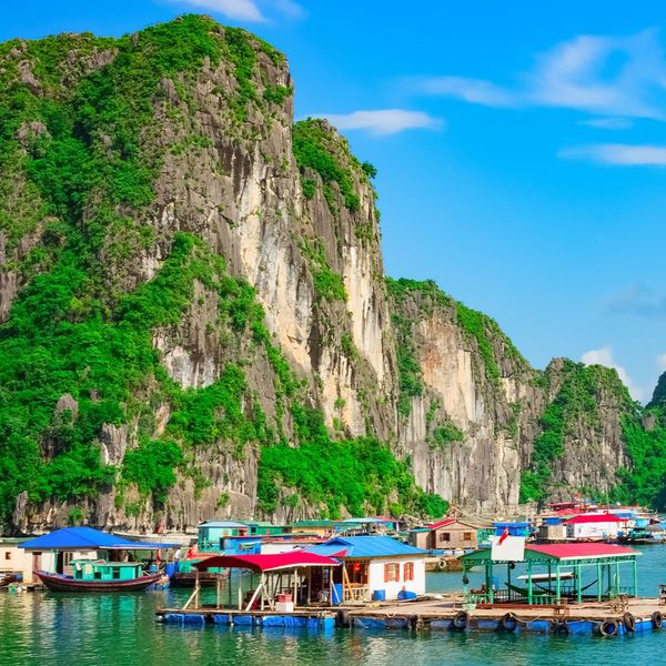 Many floating homes situated next to each other in calm waters surrounded by tall rocky islands