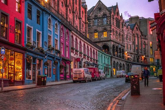 A row of vibrantly colored homes next to a street with cars parked along the side and people walking on the sidewalk