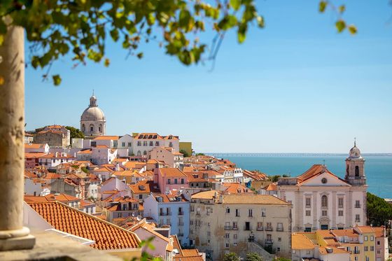 Many buildings and homes with red-tinted roofs packed tightly together and situated by the seaside with the ocean in the background