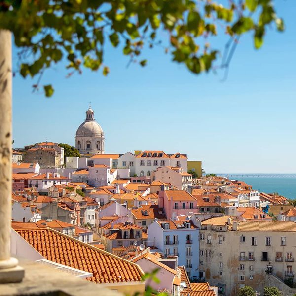 Many buildings and homes with red-tinted roofs packed tightly together and situated by the seaside with the ocean in the background