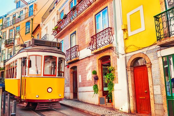 A bright yellow trolley traveling on its tracks through a colorful city street