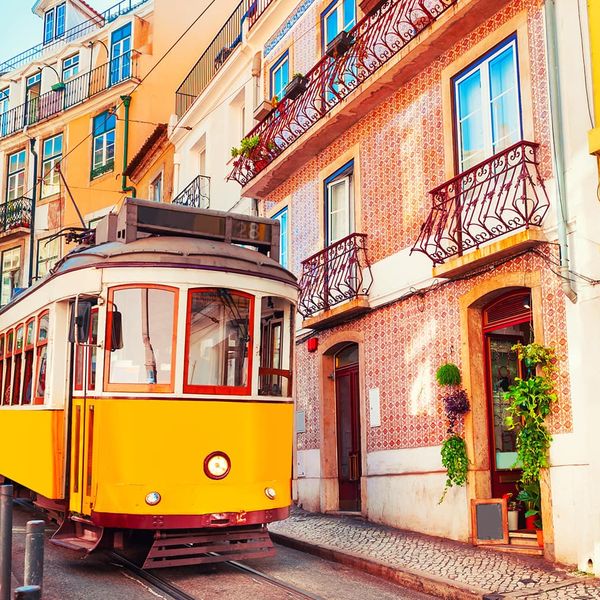 A bright yellow trolley traveling on its tracks through a colorful city street