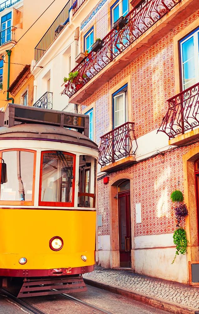 A bright yellow trolley traveling on its tracks through a colorful city street