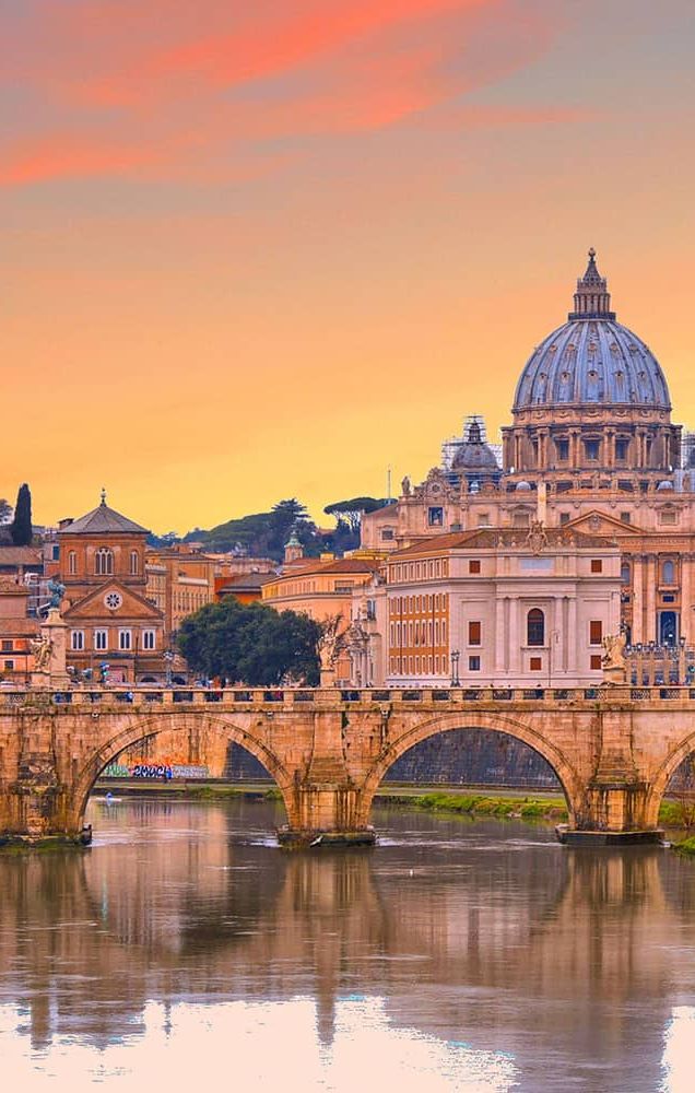 A stone bridge with a large city in the background during sunset